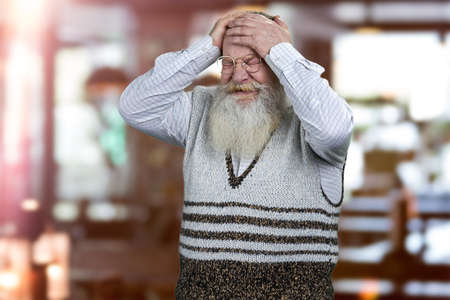 Desperate old man holding his head with frustration. Blur interior background.の写真素材
