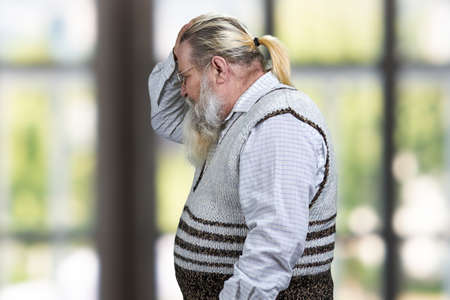 Side view of upset senior man on blurred window background.