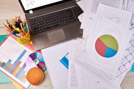 Top view laptop and many work papers with statistic diagrams. Office work desk flat lay.の写真素材