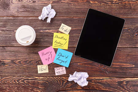 Top view flat lay tablet with sticky notes and plastic cup of coffee. Brown wooden desk background.