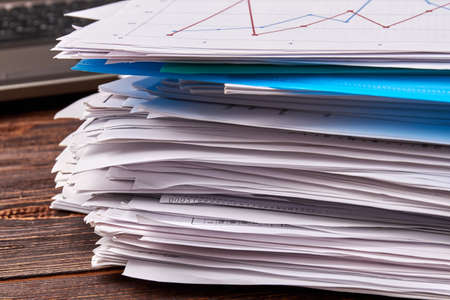 Close-up stack of office work papers on wooden desk. Paper files on the table.