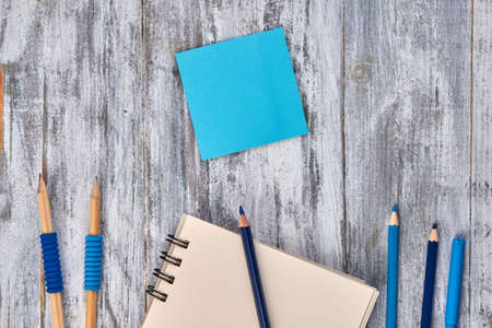 Blank blue sticky note with pencils and notepad. Gray wood background.の写真素材