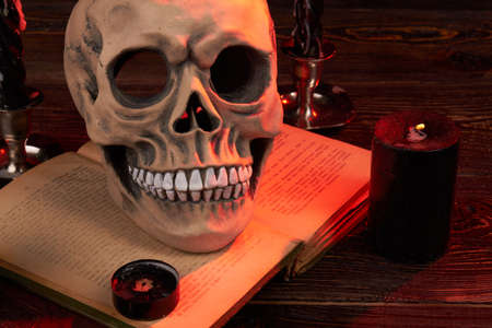 Wicca satanic ritual concept. Humans skull on the satanic bible book. Extinguished candels indoors....