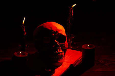 Humans skull and orange light from burning candles in the dark. Death and horror. Satanic ritual...