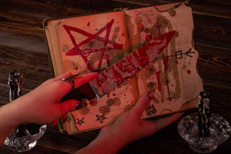Satanic wicca ritual concept. Female hand holds bloody knife over the bible with pentagram.