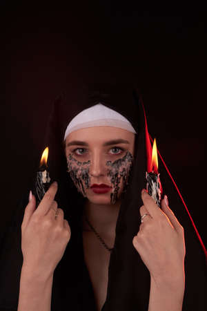 Portrait of a young gothic girl with two burning candles. Woman with creepy makeup in the dark.
