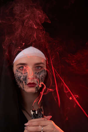 Portrait of a young girl with extinguished candles for satanic ritual . A lot of red smoke. Woman...