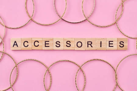 Wooden cubes with written word accessories and many golden female bangles. Womens jewelry on pink background.の写真素材
