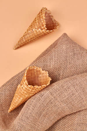 Two ice-cream cones and rustic burlap cloth on yellow background. Flat lay and top view.
