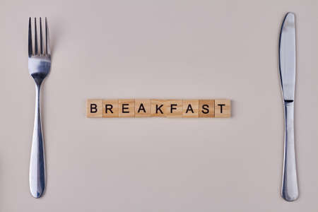Breakfast inscription from wooden blocks. Fork and knife on white background. Food concept.の写真素材