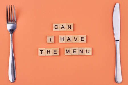 Fork, knife and text Can I have the menu written on wooden cubes. Flat lay composition on orange background.の写真素材