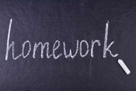 Handwritten chalk inscription homework on black chalkboard close up. Education and knowledge concept.の写真素材