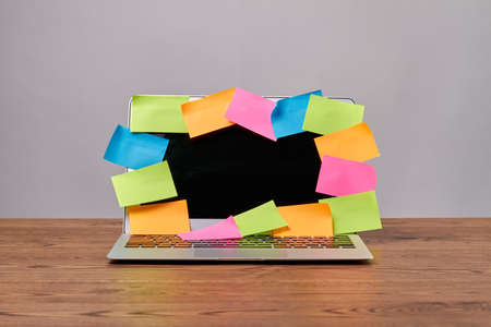 Open laptop with many colorful sticker notes for copy space. Laptop with black screen on wooden desk.の写真素材