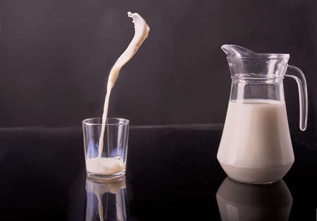 Glass jug and cup filled with white milk. Pouring organic drink in motion.の写真素材