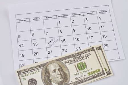 Tax deadline concept. Dollar banknotes and calendar with marked date. Top view flat lay.の写真素材
