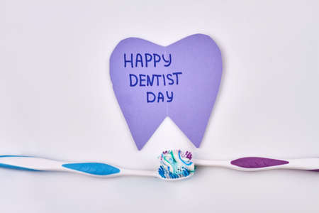 Two toothbrushes with toothpaste and happy dentist day greeting. Isolated on white background.