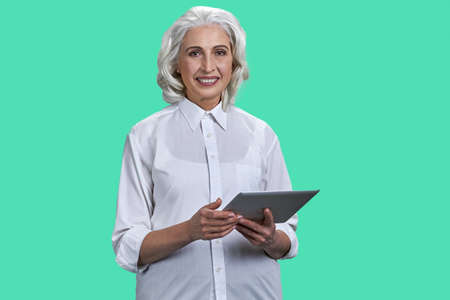 Smiling mature woman using tablet pc on color background. People and modern technology concept.の写真素材
