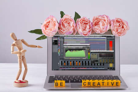 Laptop with sound editor decorated with flowers. Be creative concept. Wooden mannequin on white desk.の写真素材