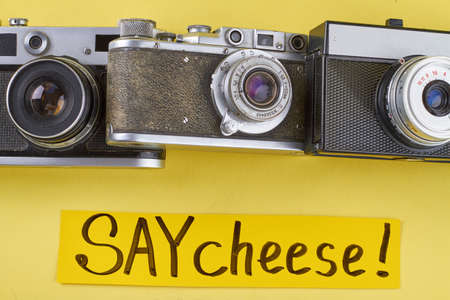 Three old retro photo camers on yellow background. Say cheese handwriting.