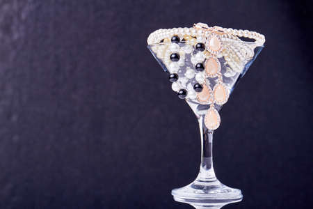 Cocktail glass full of pearls and jewelry. Close up perls on dark background.の写真素材