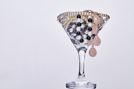 Cocktail glass full jewelry on dark background. Close up pearls in glass cup.の写真素材