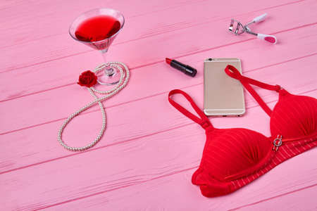 Red bra with smartphone and alcoholic drink. Top view womans accessories on pink wooden desk.の写真素材