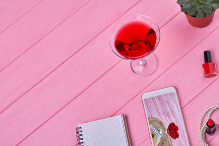 Top view female accessories on pink wooden desk. Smartphone with notepad and cocktail.の写真素材