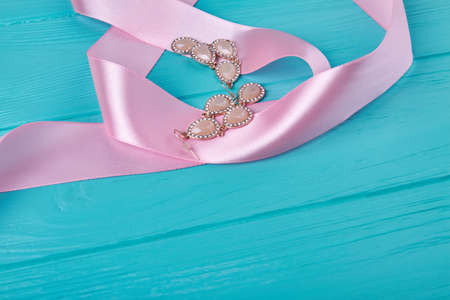 Pink ribbon and earrings on blue wooden desk. Womens accessories and copy space.の写真素材