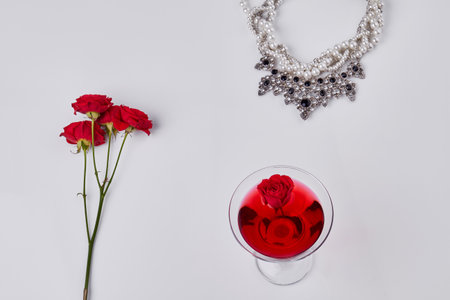 Red cocktail with rose flowers and neckalce. Top view flat lay. Isolated on white.の写真素材