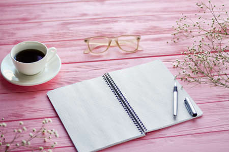 Top view blank notepad with coffee cup and glasses. Pink wooden desk.の写真素材