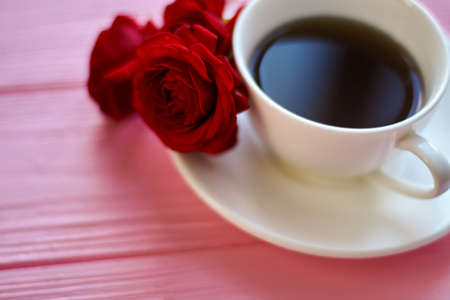Close up coffee cup with red rose flowers. Pink wood background.の写真素材