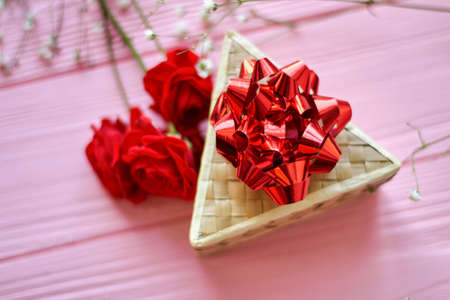 Top view triangle box with red bow. Red rose flowers on pink wooden desk.の写真素材