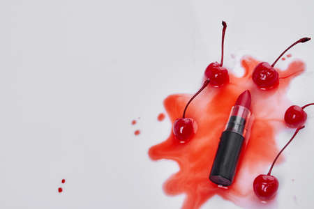 Top view lipstick and cherries on red liquid stain. Make up accessories on white background.の写真素材