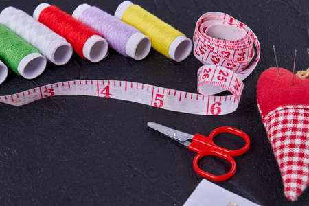Close up set of sewing accessories on dark surface. Threads with measure tape and scissors.の写真素材