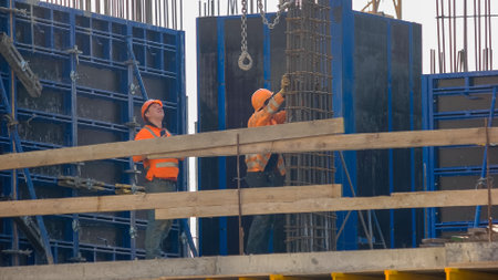 Ukraine, Kiev. 24.04.2019: Construction worker climbing on the metal frame. Two builders wearing orange clothing.のeditorial素材