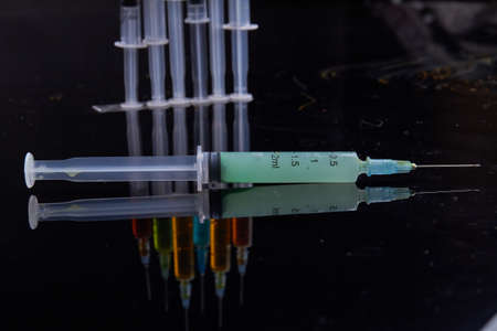 Close-up syringed fully filled with some green liquid medicine. Black reflective surface.の写真素材