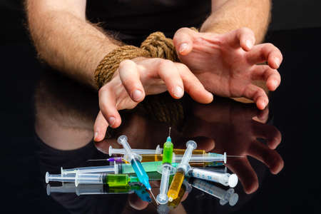 Close-up bound male hands craving for syringes filled with drugs. Drug addiction dependence and hostage concept.の写真素材