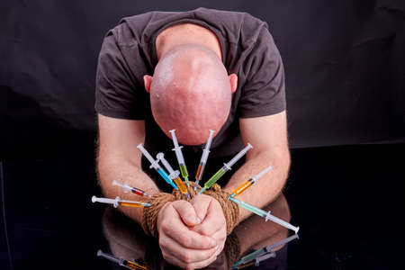 Slave of drugs concept. Man with bound hands and stucked syringes. Hostage of drugs.の写真素材