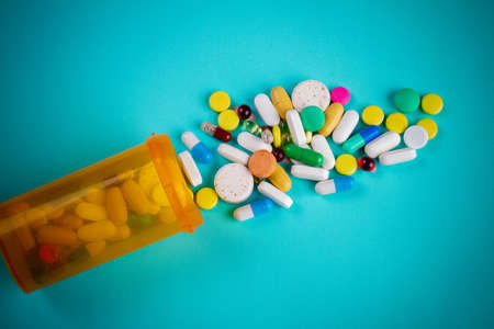 Pile of various pills from orange can on blue background. Colorful tablets and pills.の写真素材