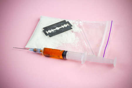 Syringe with razor and pack of powder on pink background. Drug use by injection.の写真素材