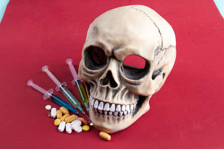Death from drugs concept. Skull with syringes and pills. Drugs and head on red background.の写真素材