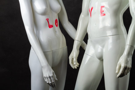 Two mannequins with love inscription on abdominal muscles. Isolated on black background.