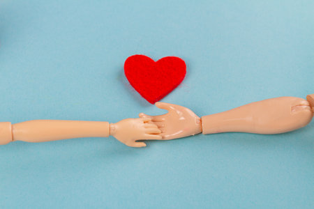 Doll hands holding and red heart on blue background. Love or charity concept.の写真素材
