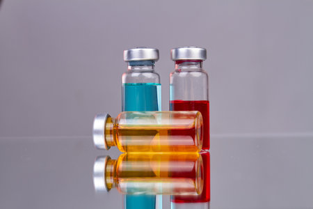 Collection of glass drug vials with colored medicine. Reflective surface with gray background.の写真素材