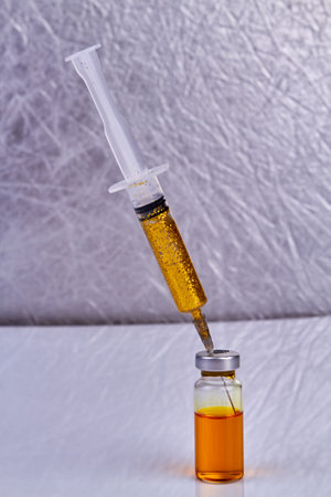 Syringe with golden glitters sticks in a vaccine bottle. Vertical shot close up.の写真素材