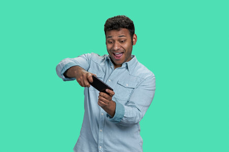 Young excited indian man playing videogame on mobile phone. Isolated on green.