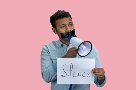 Indian man taped mouth speaks in megaphone. Censorship and free speech concept. Isolated on pink.の写真素材