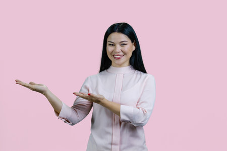 Young cheerful asian woman open hand palms with copy space for product. Isolated on pink background.の写真素材