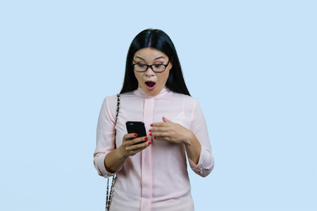 Portrait of an extremely shocked and surprised young asian businesswoman with smartphone. Isolated...