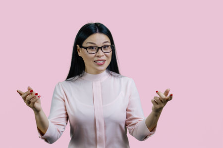 Young asian woman is gesturing actively with both hands. Isolated on pink.の写真素材